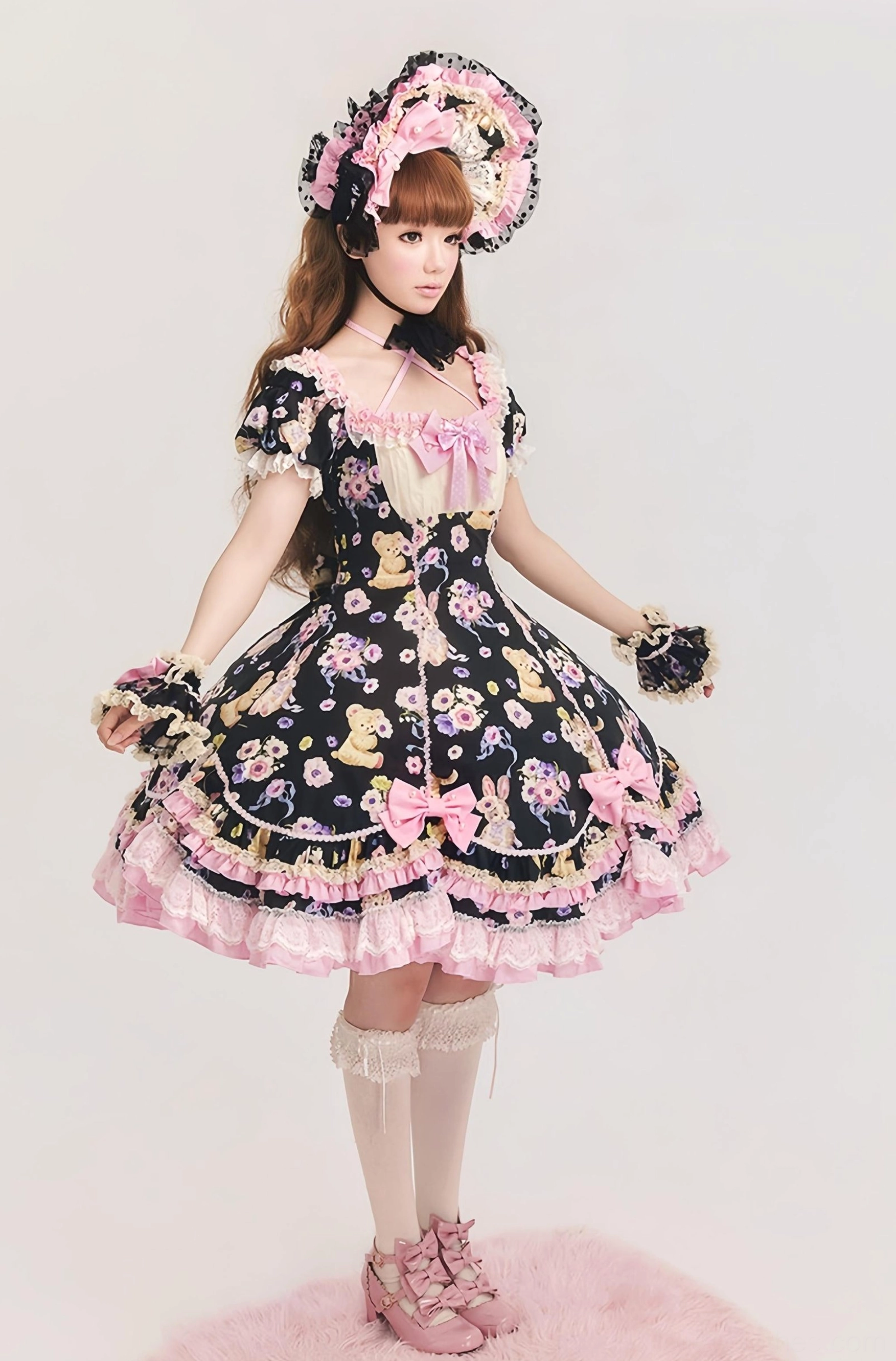 Full-body front view of black sweet lolita OP dress with teddy bear and floral prints, featuring pink ruffled lace trims, matching bonnet and gloves, displayed on pink fluffy studio rug