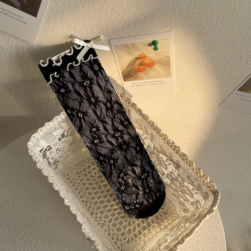 Black floral lace Lolita ankle socks with yellowish ribbon bow accent featuring sheer lace texture and ruffled sock opening on model