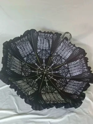 Black gothic lace-print Lolita umbrella with all-over vintage pattern and ruffled canopy edge on white studio backdrop, overhead flat lay capturing ornate details