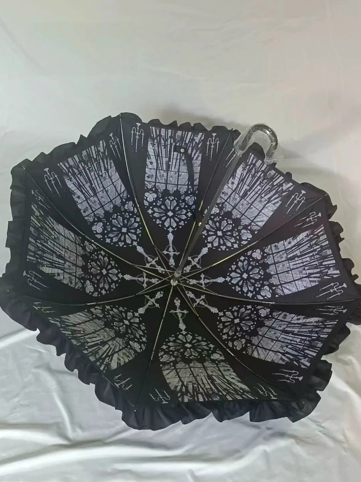 Black gothic lace-print Lolita umbrella with all-over vintage pattern and ruffled canopy edge on white studio backdrop, overhead flat lay capturing ornate details