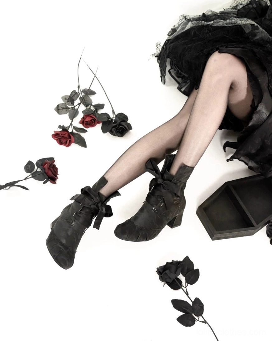 Black lolita ankle boots side low angle leg shot showcasing ribbon bow ankle straps block heel matte black suede fabric finish on white studio background with rose decorations