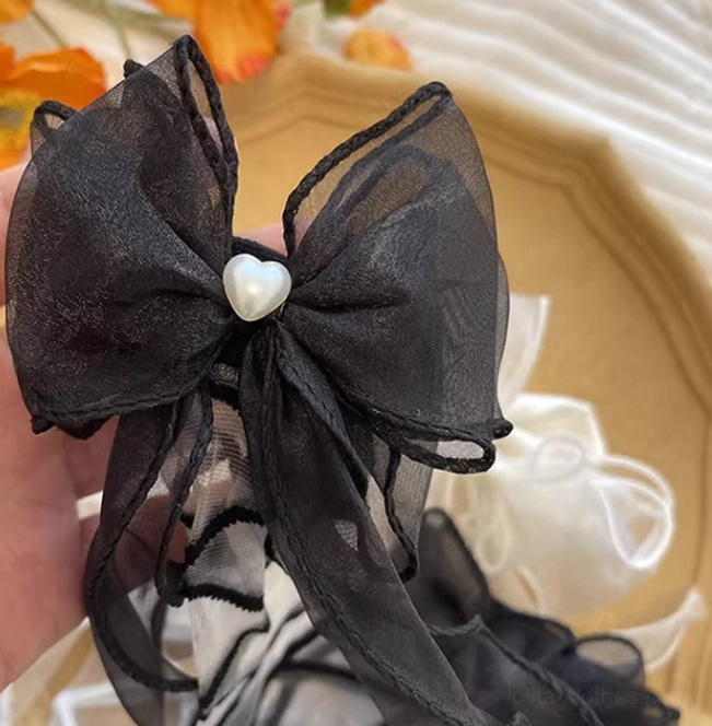 Close-up flat lay detail shot of single black lolita gauze ankle sock featuring organza bow with pearl and heart center and delicate sheer crisscross strap on decorative tray