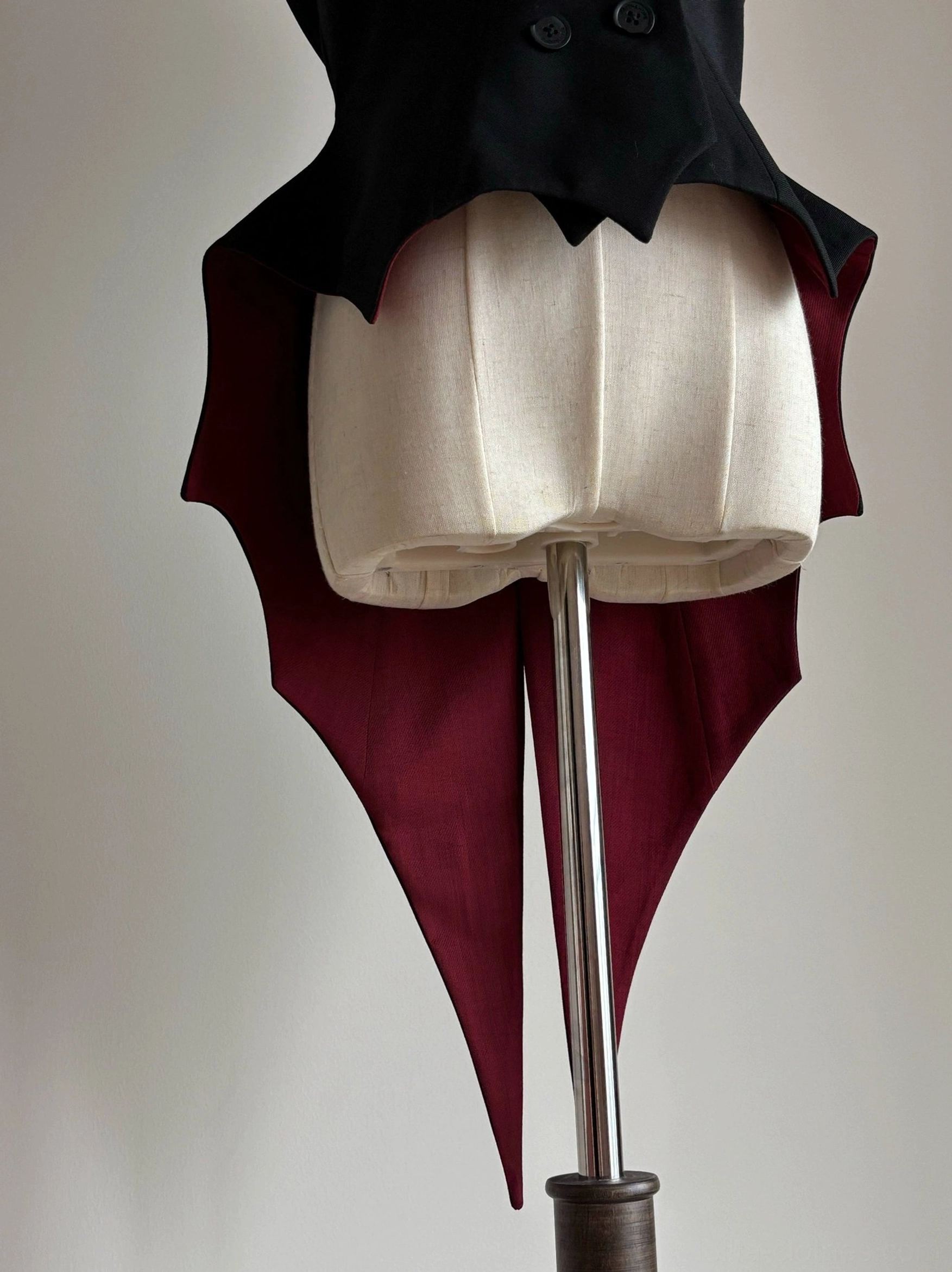 Black sleeveless Gothic Lolita waistcoat with wine-red bat-wing tail hem displayed on dress form showing overall silhouette and hem panel positioning