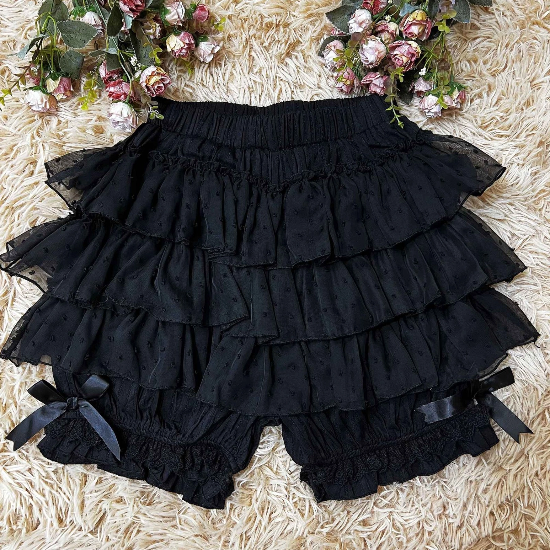 Black layered lolita bloomers with sheer ruffled tiers and black satin bows on leg cuffs shown on fluffy carpet background