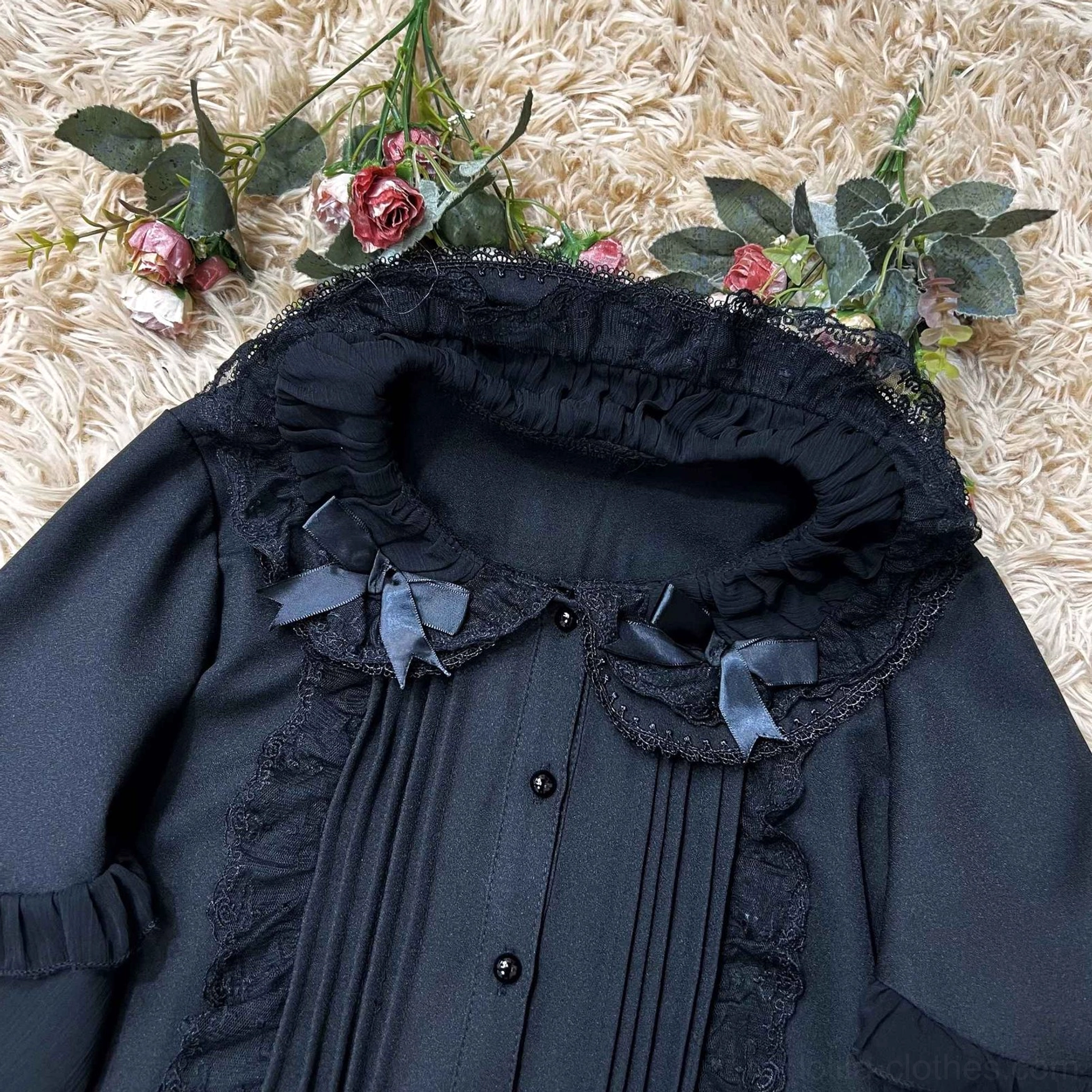 Close-up flat lay detail of black Lolita blouse's ruffled Peter Pan collar, tiny satin bow embellishments and front button placket on floral decorated background