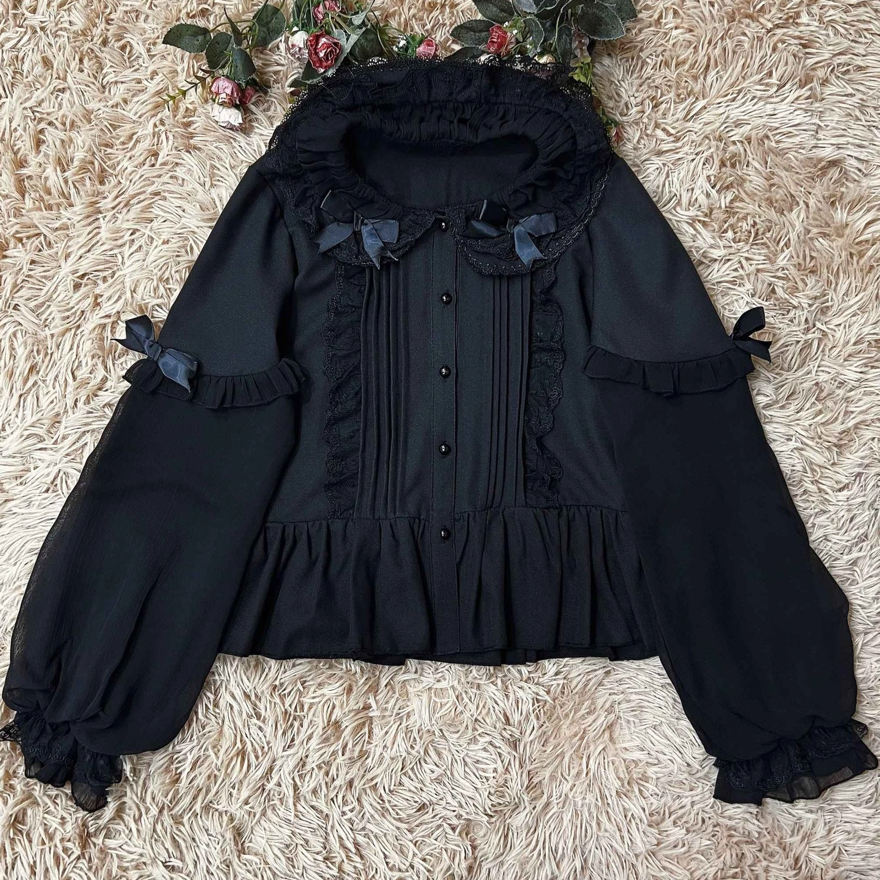 Full flat lay view of black Lolita blouse showing complete silhouette with double-layered puff sleeves, ruffled collar with bow accents and front lace details on fluffy fur background