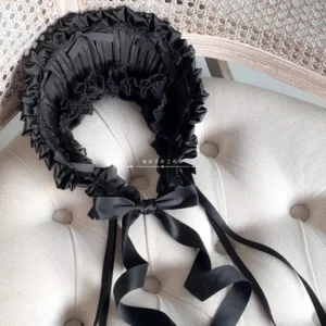 Black lolita bonnet flat lay top-down view showing pleated ruffled edges and central black bow with trailing ribbons