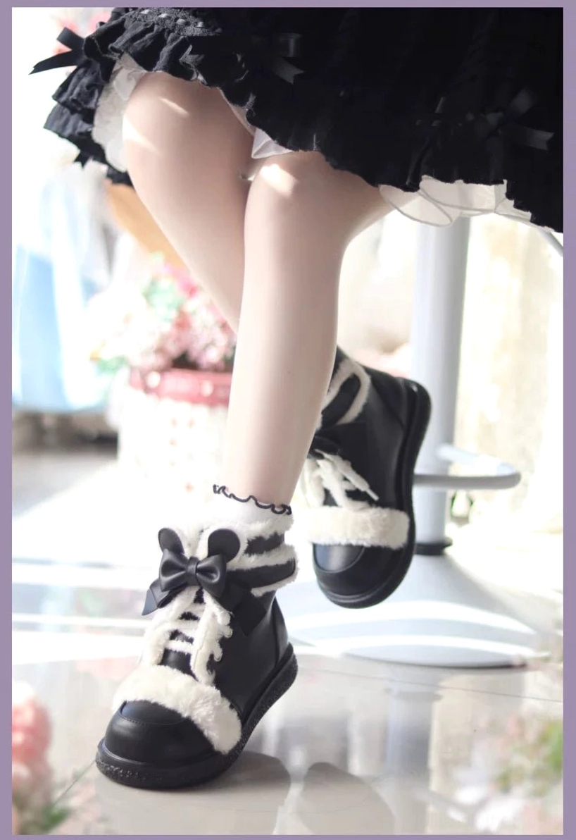 Black and white lolita winter ankle boots with black leather upper, white plush trim, and large black bow laces, low frontal wearing view with black ruffled skirt
