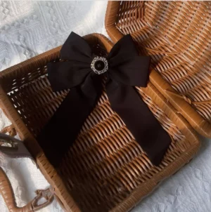 Black Lolita bow hair clip with vintage rhinestone buckle displayed on wicker picnic basket with knitted background
