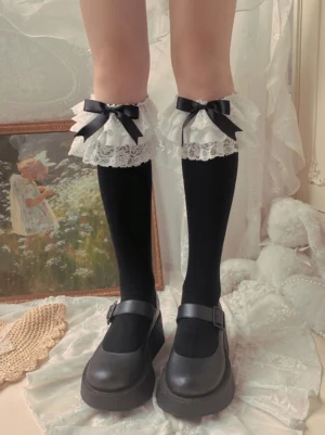 Black cotton Lolita mid-calf socks with white layered ruffled lace trim cuff and black satin bow accents paired with black platform Mary Jane shoes vintage bedroom setting