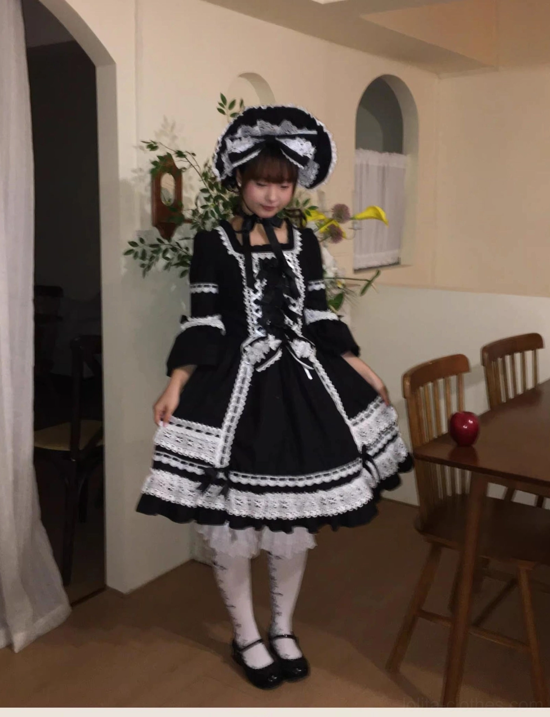 Detail photograph of white lace-up front panel of black lolita dress with decorative bow, showing intricate lacing through delicate tulle construction