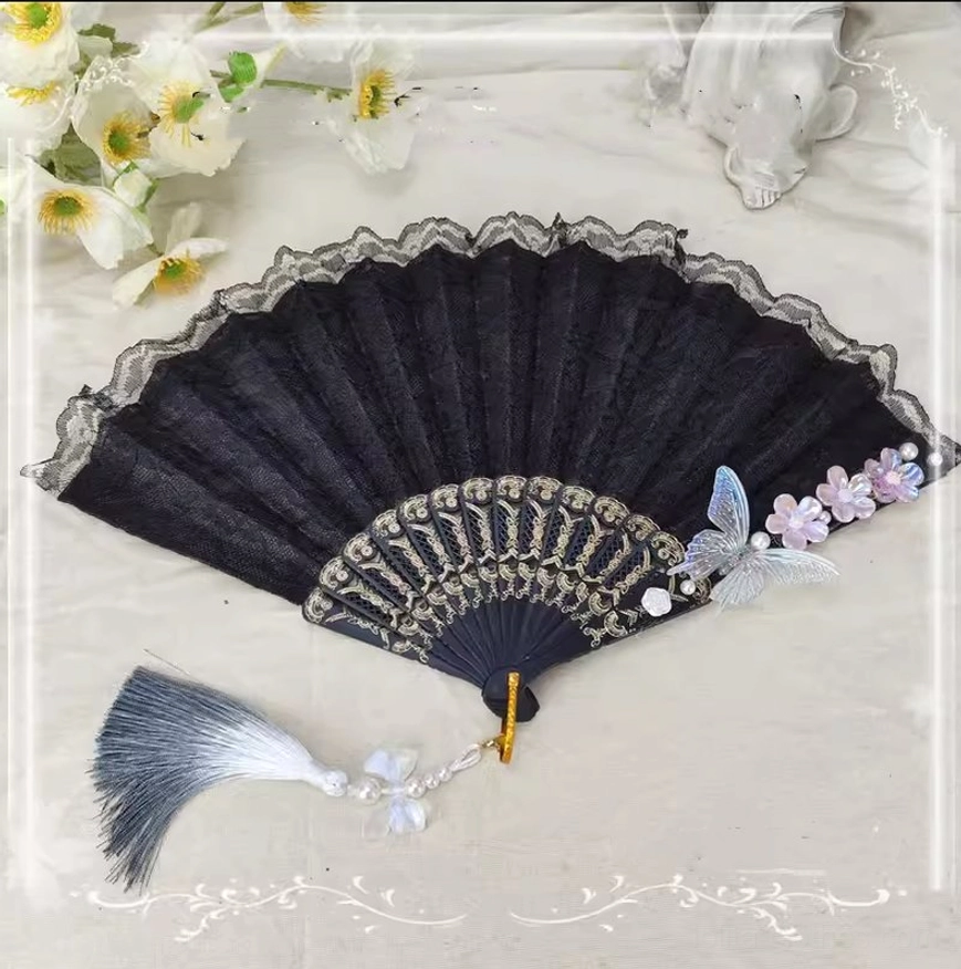 Black lolita folding fan with lace overlay featuring blue butterfly and purple gradient flowers with grey tassel and pearl pendant displayed on linen fabric