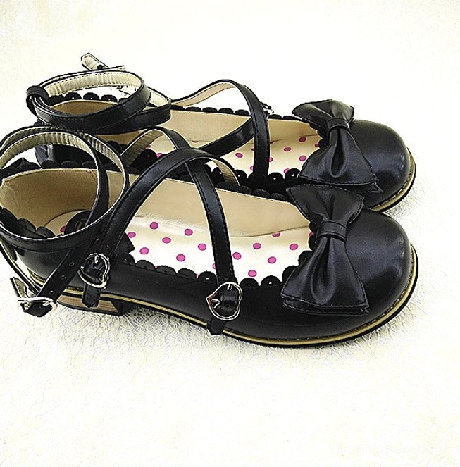 Black Lolita low heel princess Mary Jane shoes featuring cross ankle straps with metal buckles, large black bow front decoration, scalloped shoe trim, and polka dot inner sole