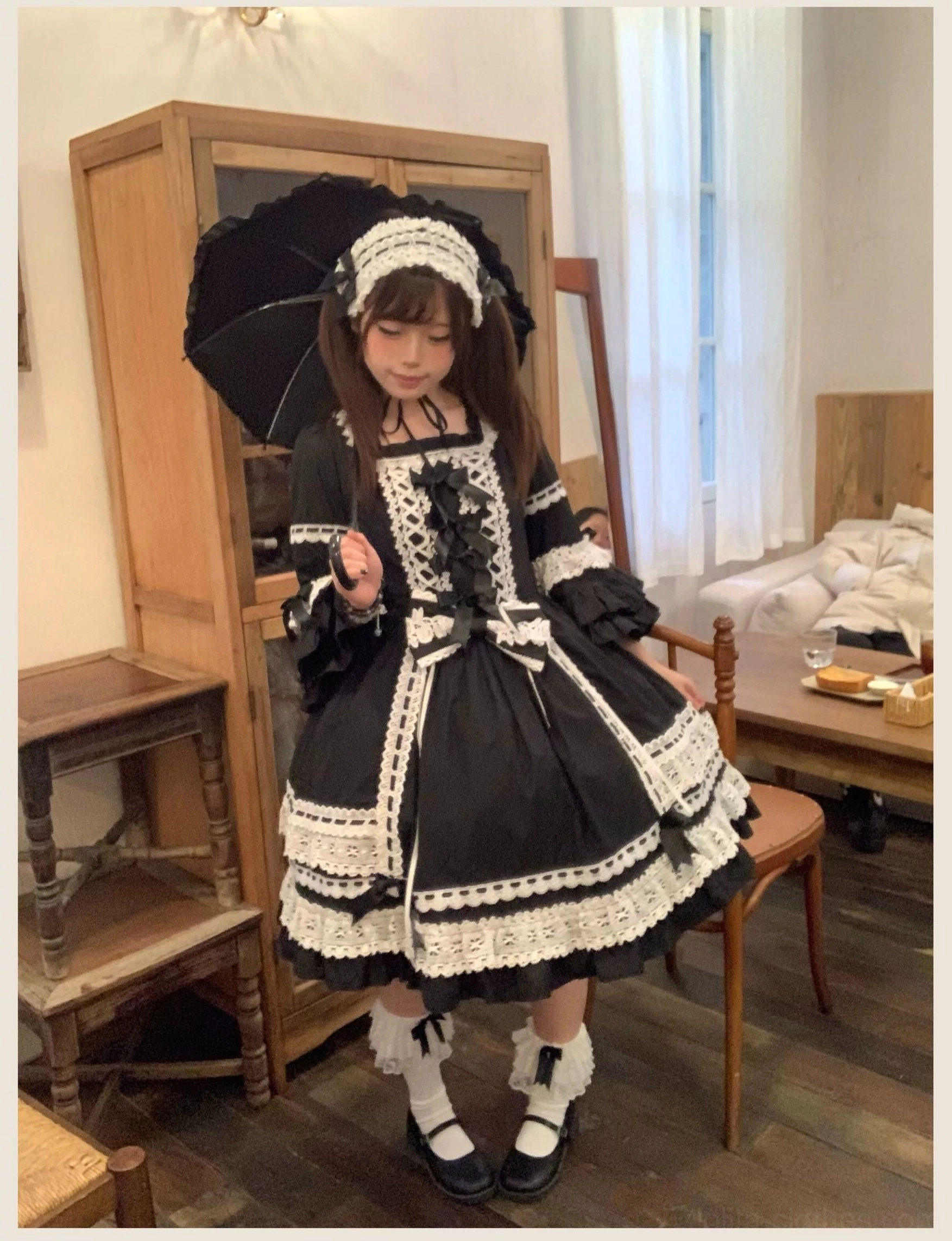 Black lolita OP dress with matching bonnet worn in vintage indoor dining room setting with black lace umbrella, paired with white frilly socks and black Mary Jane shoes