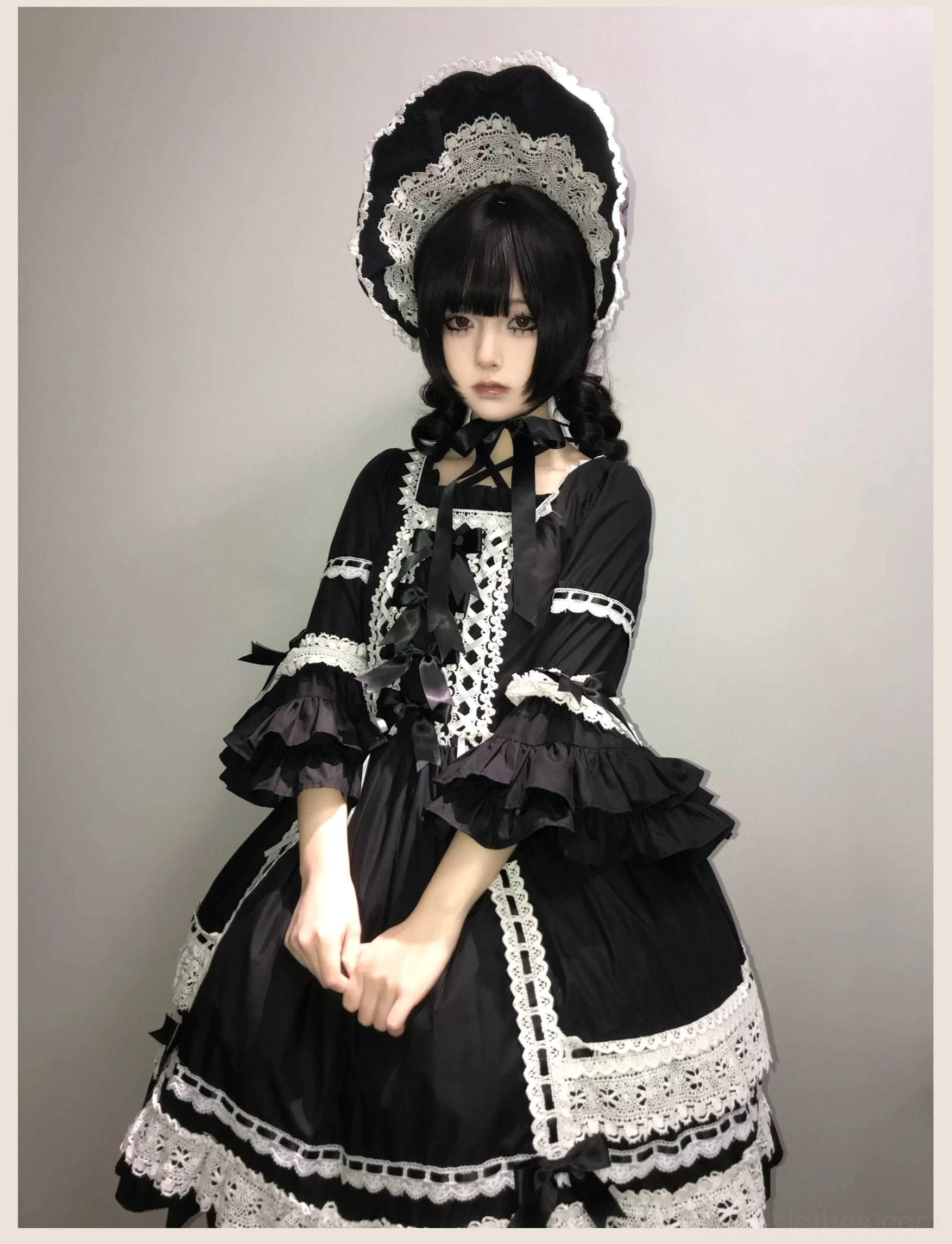 Front studio shot of black lolita one-piece dress with white lace trims, ruffled puff sleeves, waist bow, and A-line skirt silhouette with matching bonnet