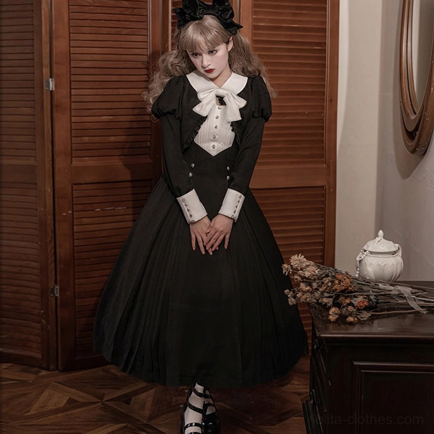 Full front standing view of black Gothic Lolita OP dress with floor-length pleated skirt, white Peter Pan collar, bow tie, and cuffed puffed sleeves, model wearing platform shoes