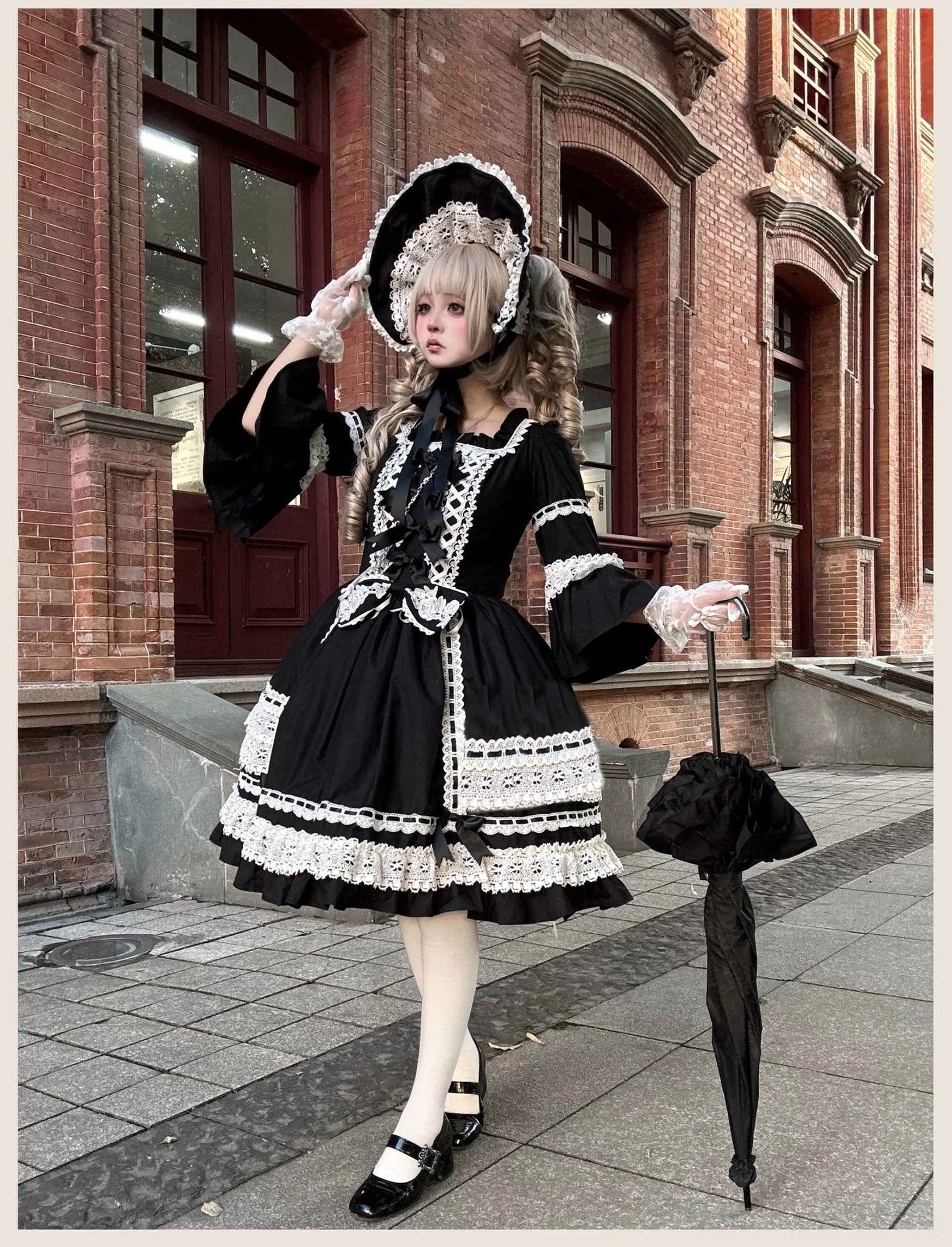 Three-quarter view of black old school lolita dress with puffed bell sleeves, white lace trim, waist bow, and layered skirt held with black umbrella outdoors