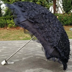 Black foldable lolita sunscreen parasol with small bow decorations and scalloped lace ruffled edge, displayed fully opened in outdoor garden setting showing elegant side profile view