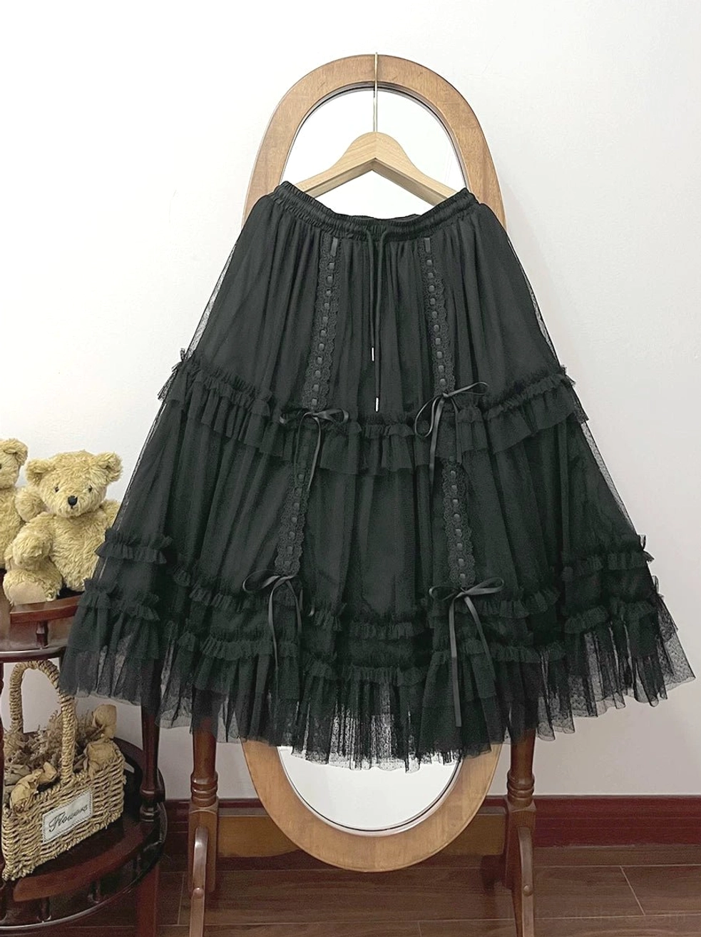 Black lolita tulle underskirt with tiered ruffled layers and bowknot ribbon accents, hanging on vintage wooden hanger with mirror, displaying drawstring adjustable waist