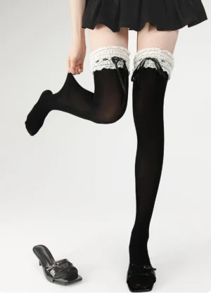 Black lolita socks side dynamic view with one leg lifted, paired with black pleated skirt and flat shoe, demonstrating over-the-knee coverage
