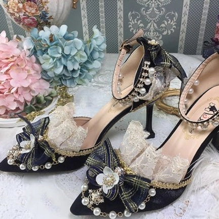 Black pointed toe Lolita wedding heels overhead flat lay view with hydrangea flower decorations, showing black suede upper, gold edge trim, pearl-decorated black bow, pearl ankle strap, and thin stiletto heel