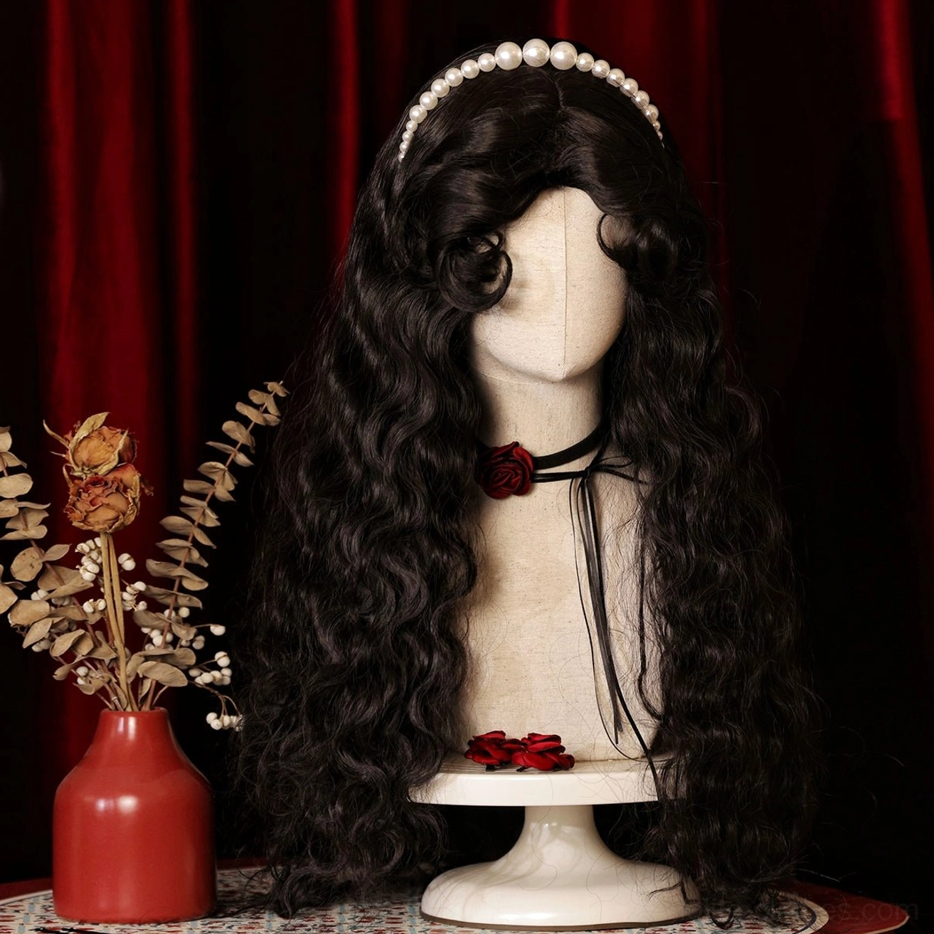 Side back view of long voluminous black curly Lolita wig with black rose choker on mannequin against red velvet and patterned fabric