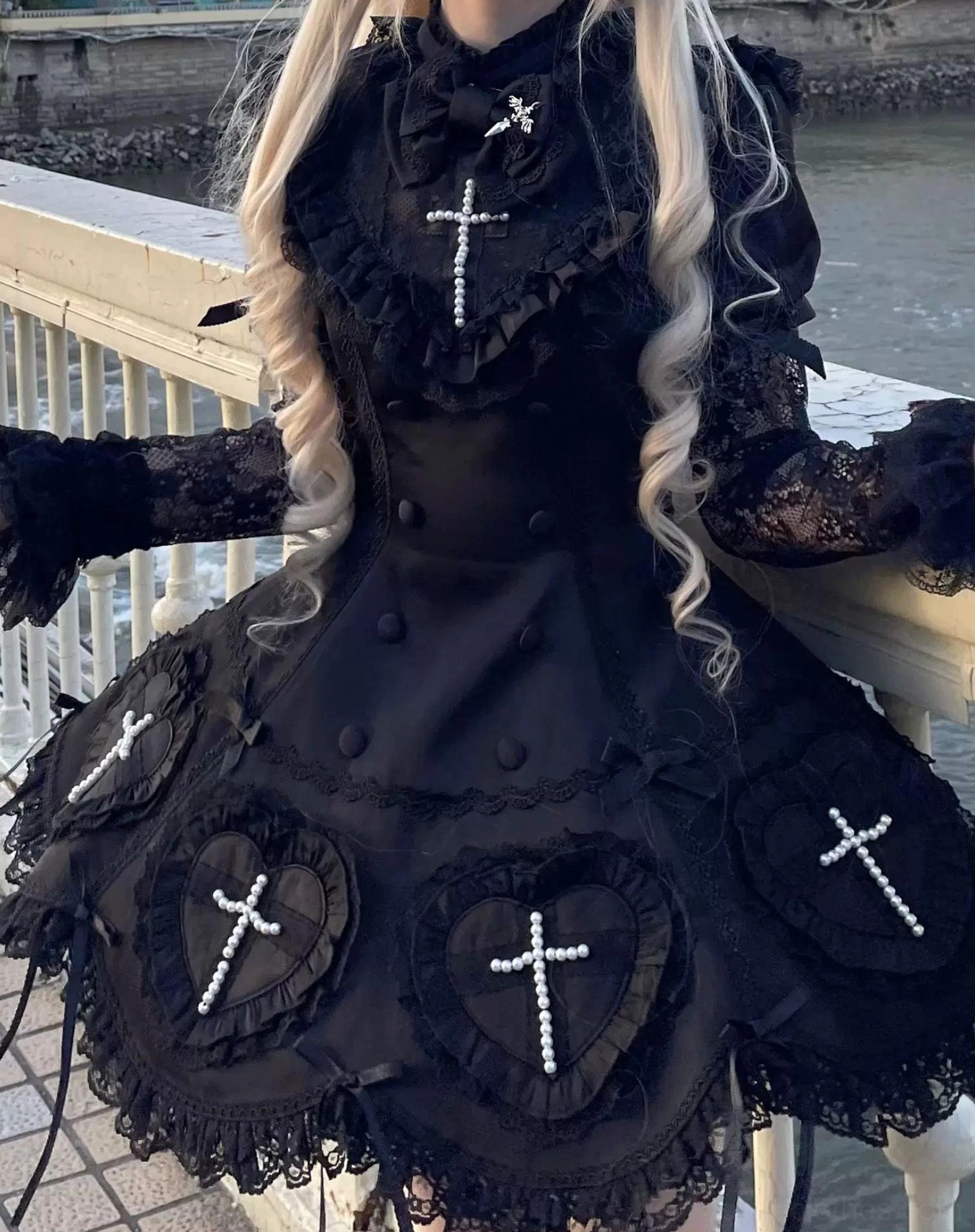 Black Nocthymn Cross Gothic Lolita dress back half view outdoor riverside showing long blonde hair lace gloves heart cross patches on skirt bodice