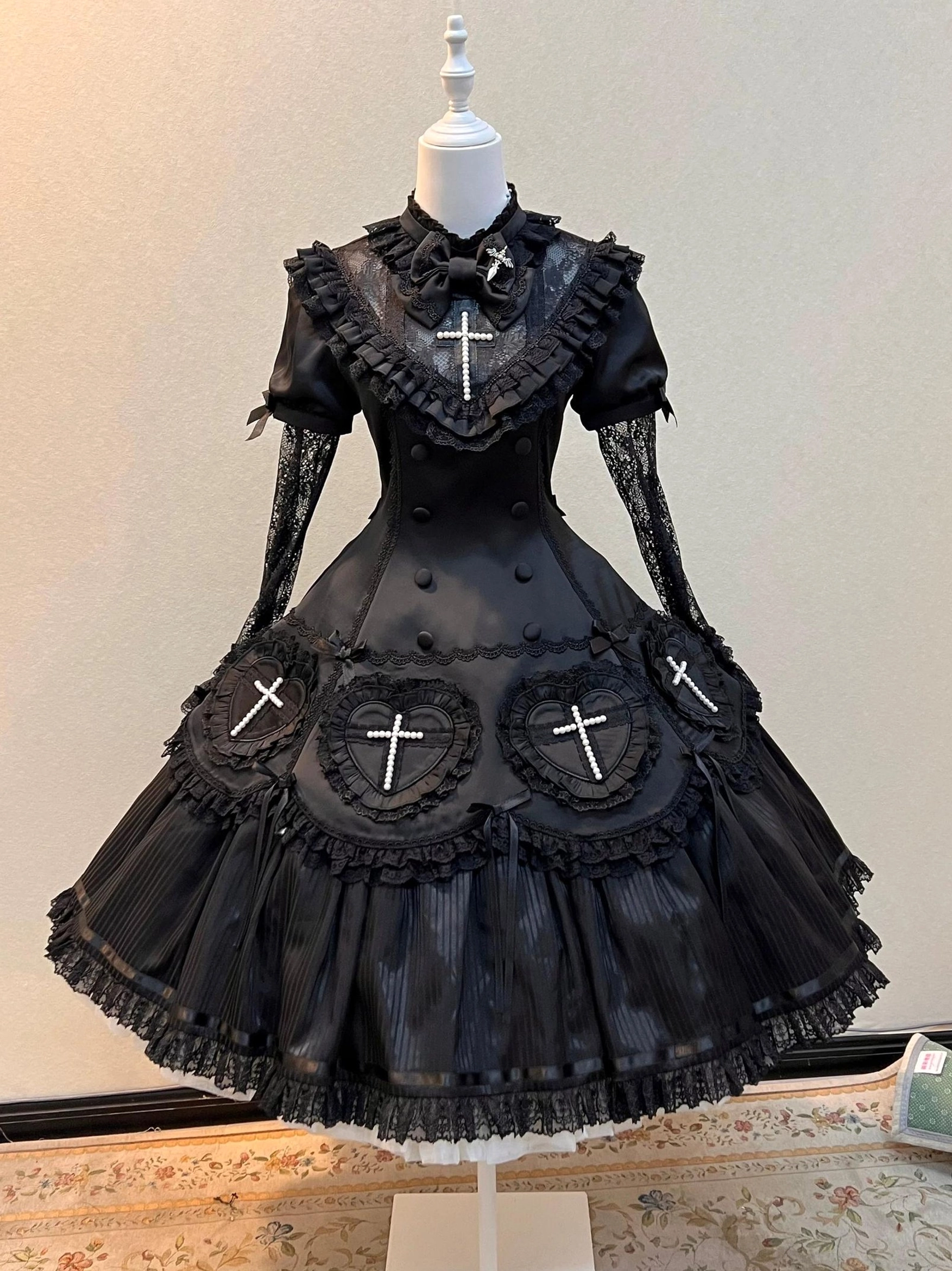 Black Nocthymn Cross Gothic Lolita OP dress front full view on dress mannequin featuring pearled heart cross details and layered ruffled skirt