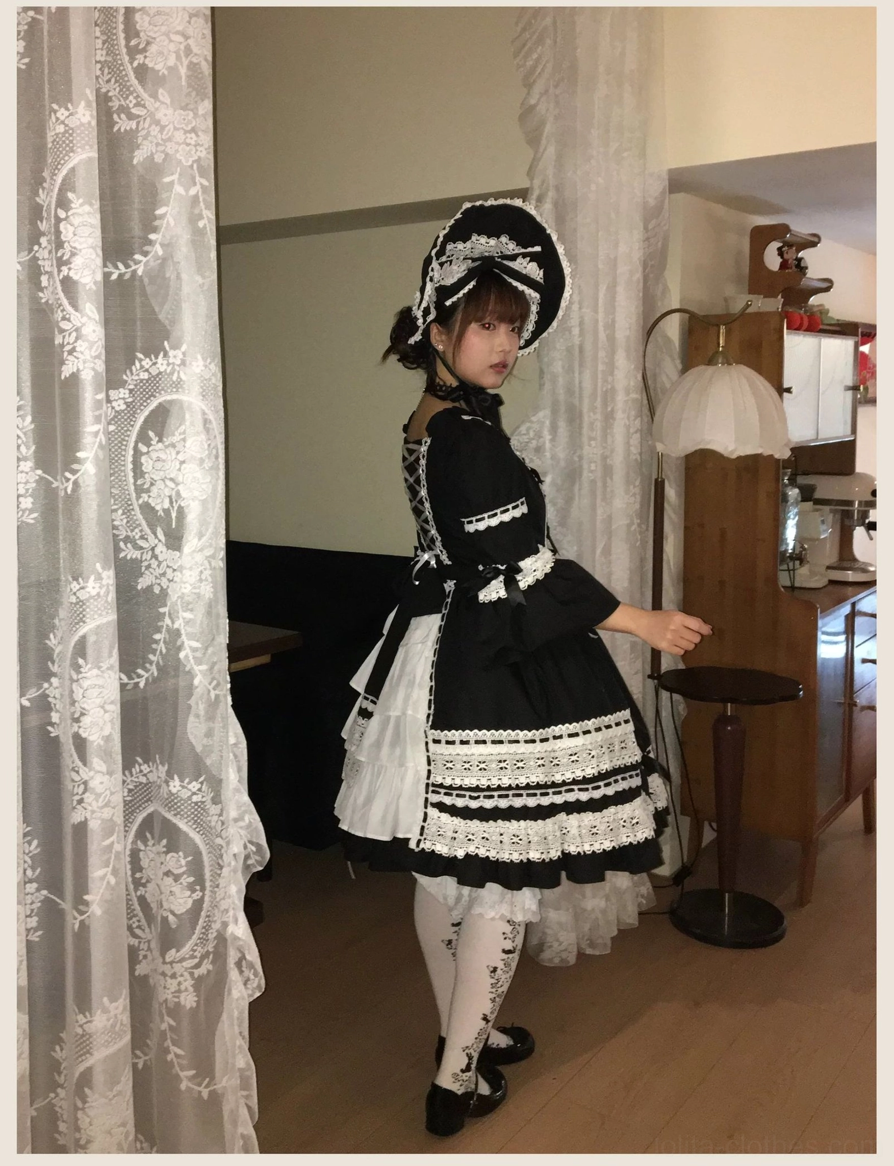 Studio full body shot of black old school lolita OP dress with matching bonnet, showing front bow accent, puff sleeves, and complete vintage silhouette profile