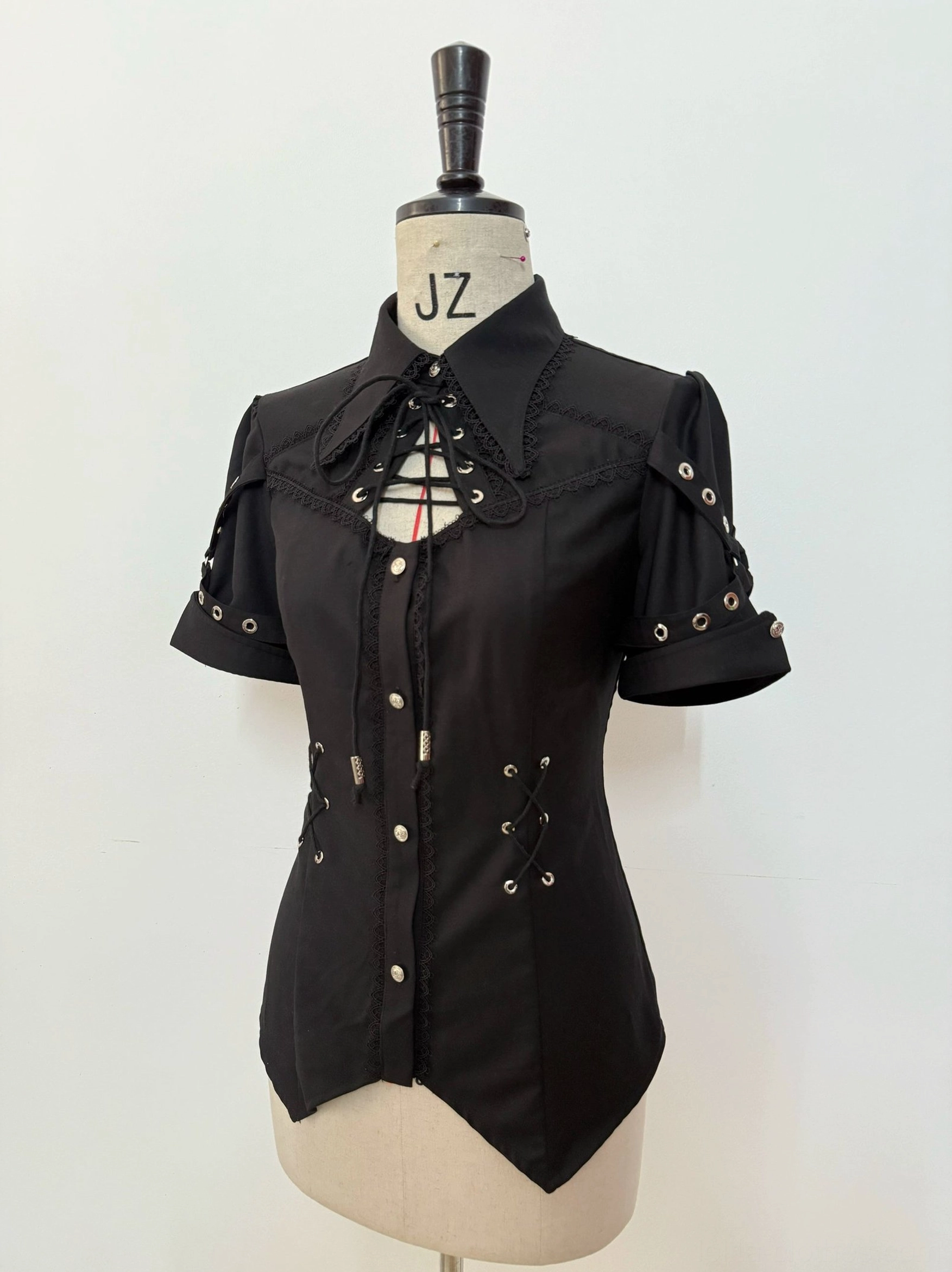 Black Ouji Lolita blouse front view on dress mannequin featuring chest cutout with lace-up trim, buttoned front closure, decorative lace-up accents on short sleeves, fitted tailored silhouette with pointed hem and prince-style lapel collar