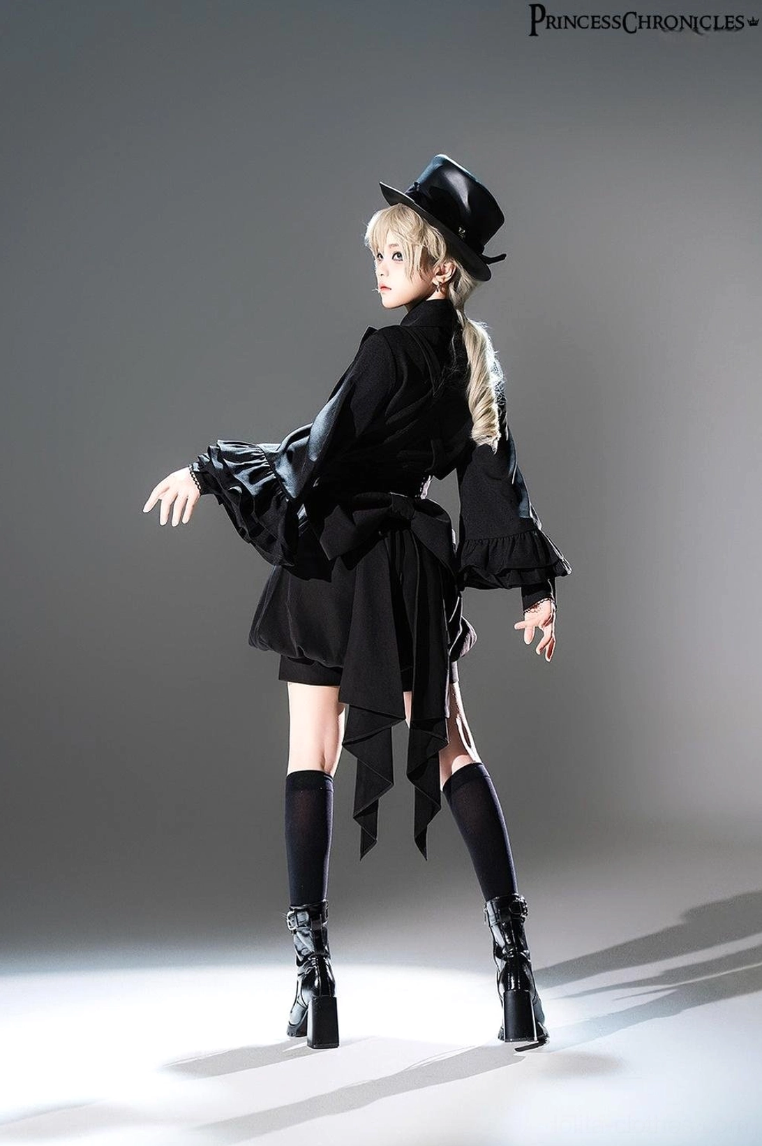Rear view of black Ouji Lolita outfit showing detachable large back bow sash, tailored waistline, voluminous bishop sleeves, and structured silhouette from behind
