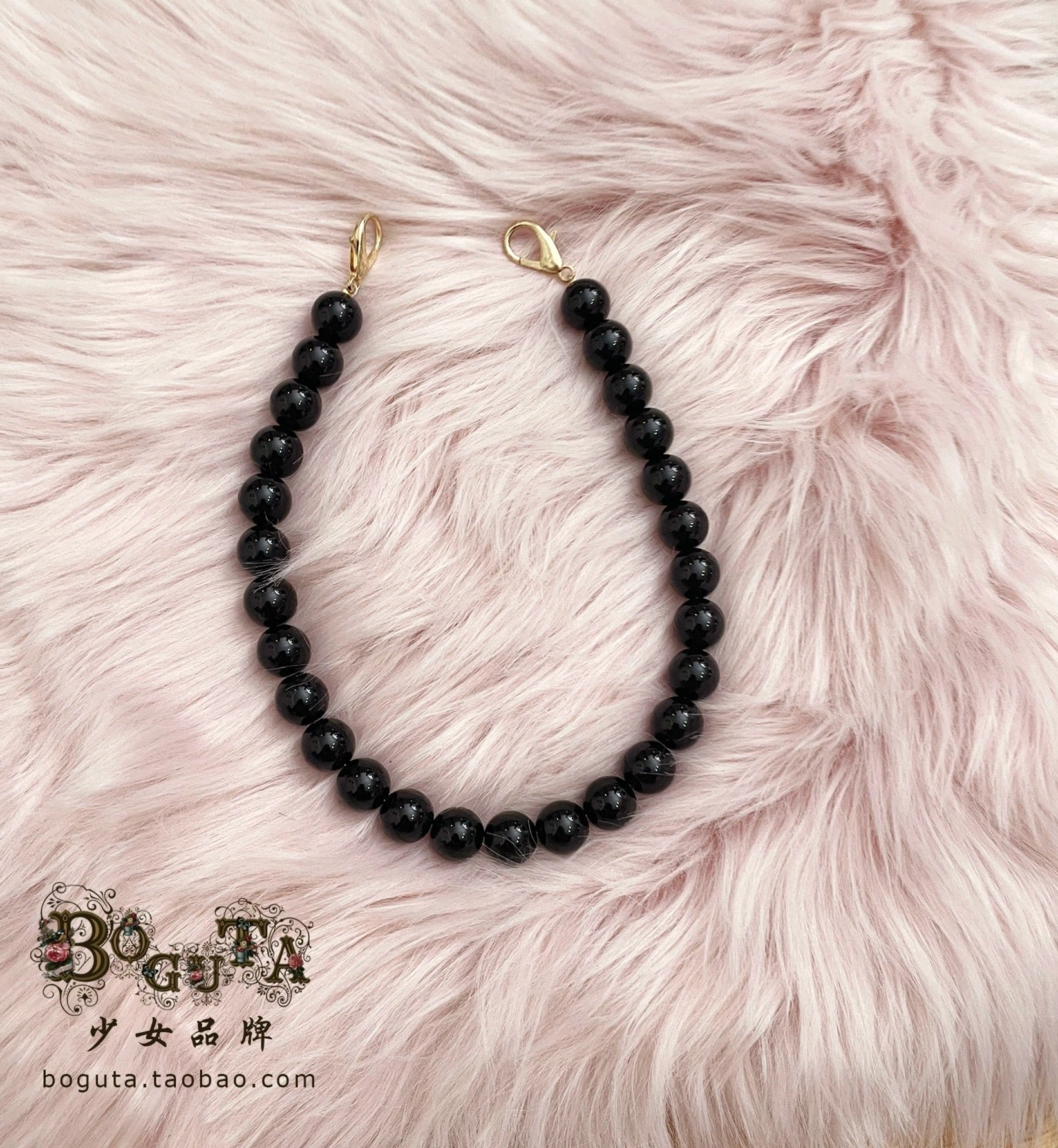 Single black matte bead handheld bag chain strap 40cm length with gold lobster clasp connectors on pink fuzzy fur background showing glossy finish detail