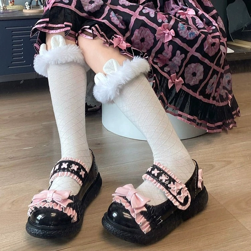 Lower body close-up view of black-pink Lolita flat shoes on wooden floor, featuring black patent leather with pink satin bow decor and star printed ruffled straps