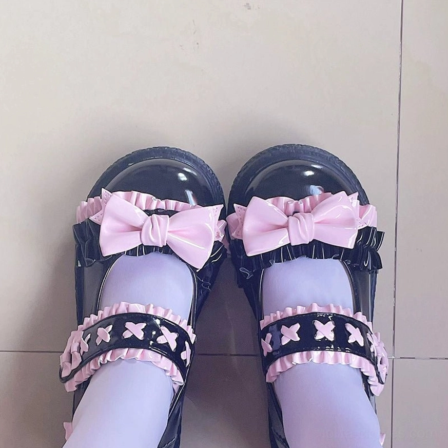 Overhead flat lay of black-pink Lolita flat shoes on tiled floor with light purple stockings, single ruffled star strap with large pink satin bow and low platform sole