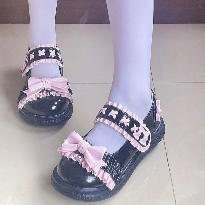 Front and side close-up view of black-pink Lolita flat shoes on feet with light purple stockings, featuring large pink satin bow and ruffled star motifs on thick platform sole
