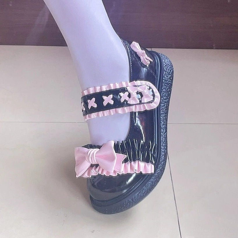 Side close-up of black-pink Lolita flat shoes on foot against tiled floor with light purple stockings, pink ruffled star buckle strap and pink toe bow detail