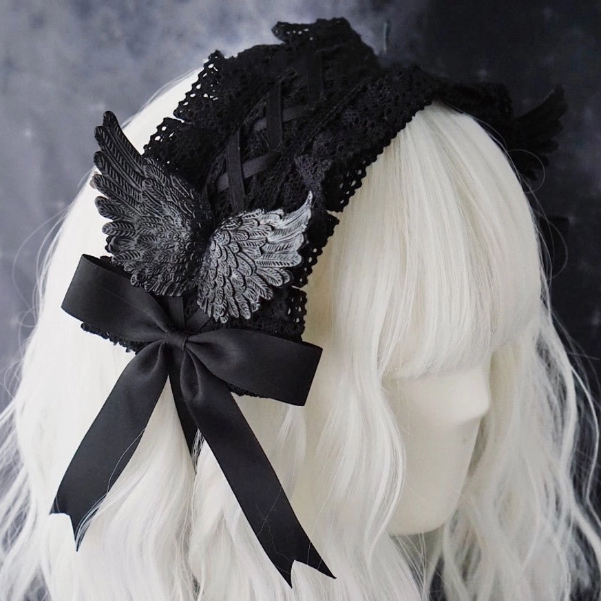 Black gothic raven wing lolita hairband with large satin bow and silver-black wing ornaments displayed on white mannequin head showing crossover strap design