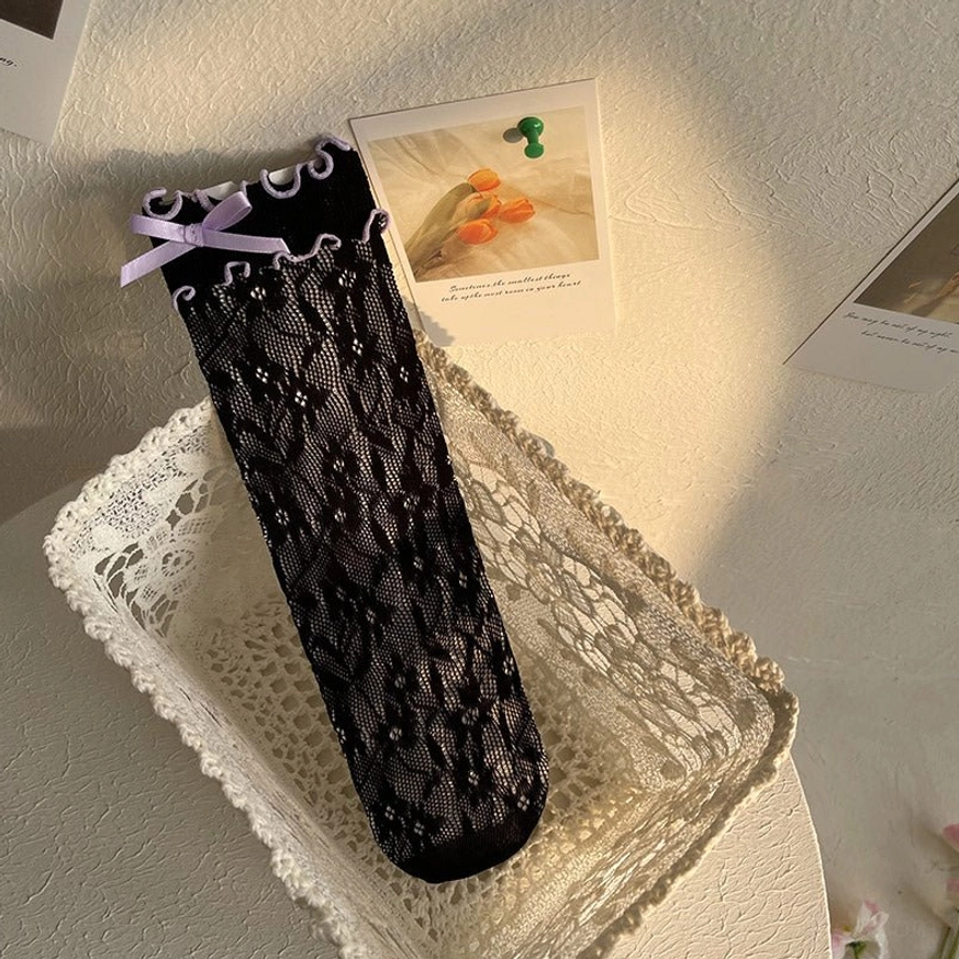 Black ruffled lace ankle socks with purple ribbon bow accent showing delicate lace weave and sweet ruffled sock opening trim on model's leg