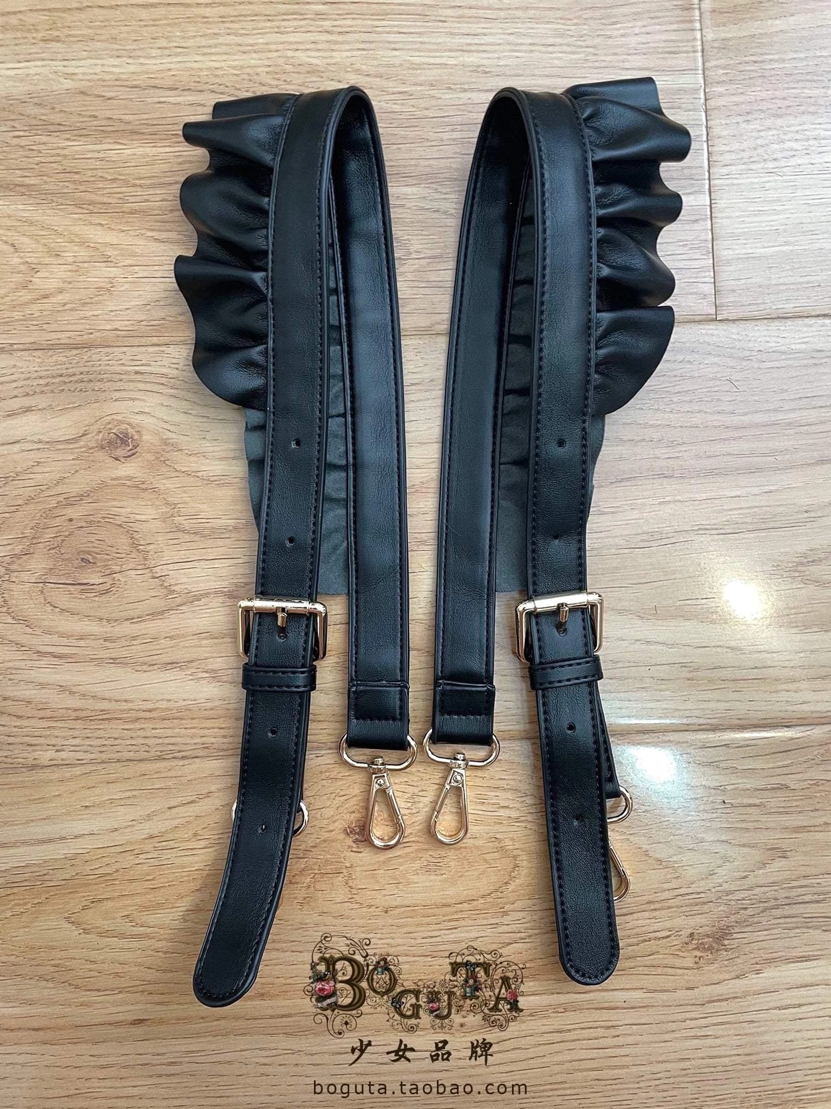 Black ruffled PU leather lolita bag shoulder straps pair with smooth material and gold-tone metal hardware on warm wooden background perfect for gothic coordinates