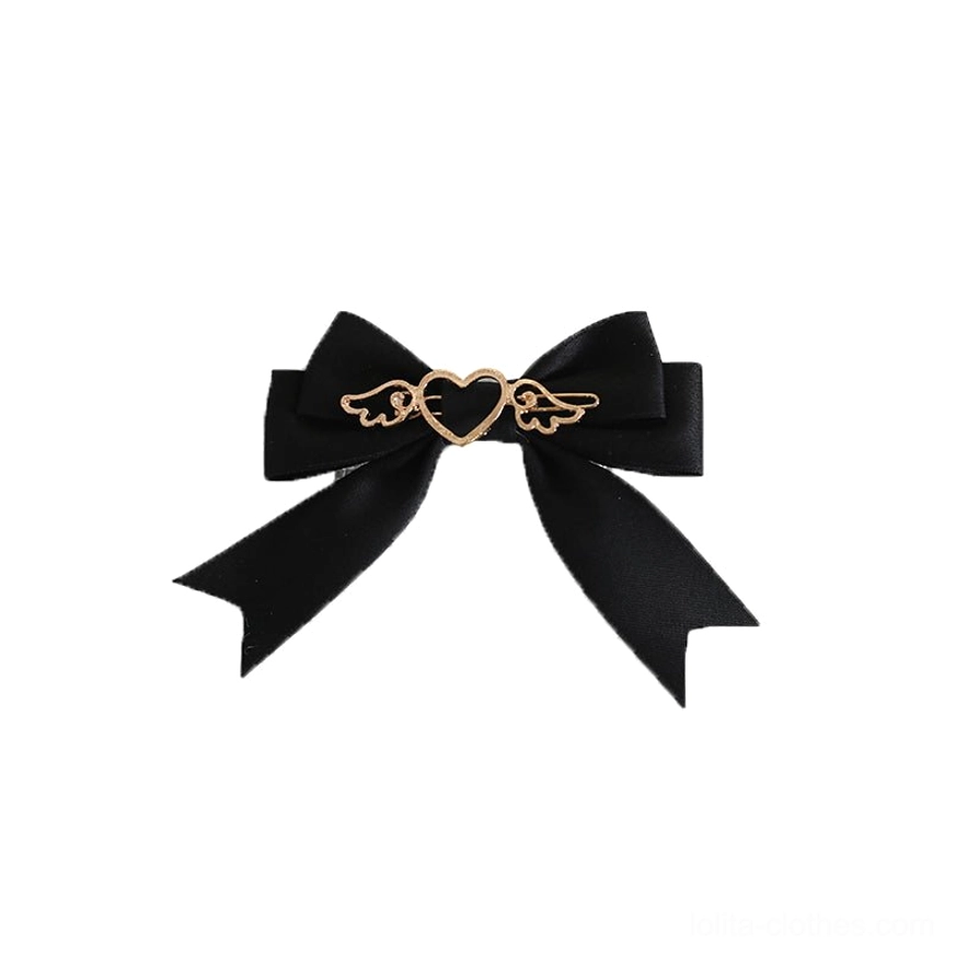 Black satin lolita bow hair clip with gold heart-wing metal charm and neat ribbon tails flat lay view