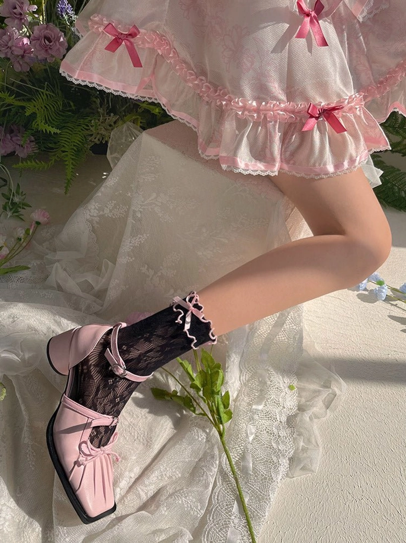 Black sheer lace Lolita ankle socks with ruffled cuff and pink square-toe Mary Jane shoes displayed on model's lower legs with floral greenery background