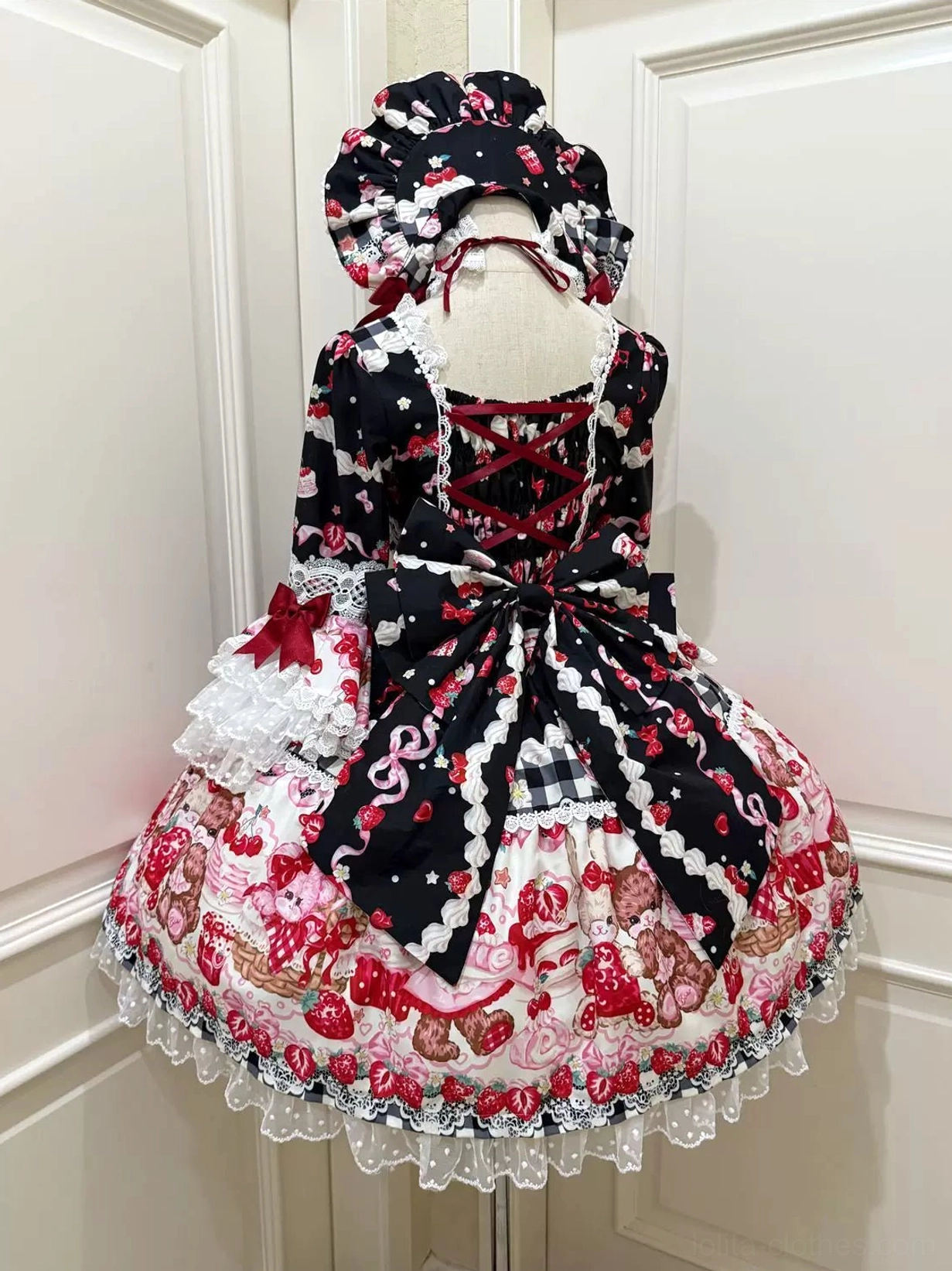 Black strawberry bear print sweet lolita one-piece dress back view on mannequin with crisscross lace-up construction, black satin waist bow, ruffled hem and matching bonnet