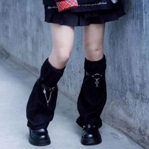 Black suede gothic leg covers with silver cross pendant worn on model's lower legs in outdoor concrete setting, paired with punk casual outfit featuring loose suede fabric texture and adjustable buckle strap visible
