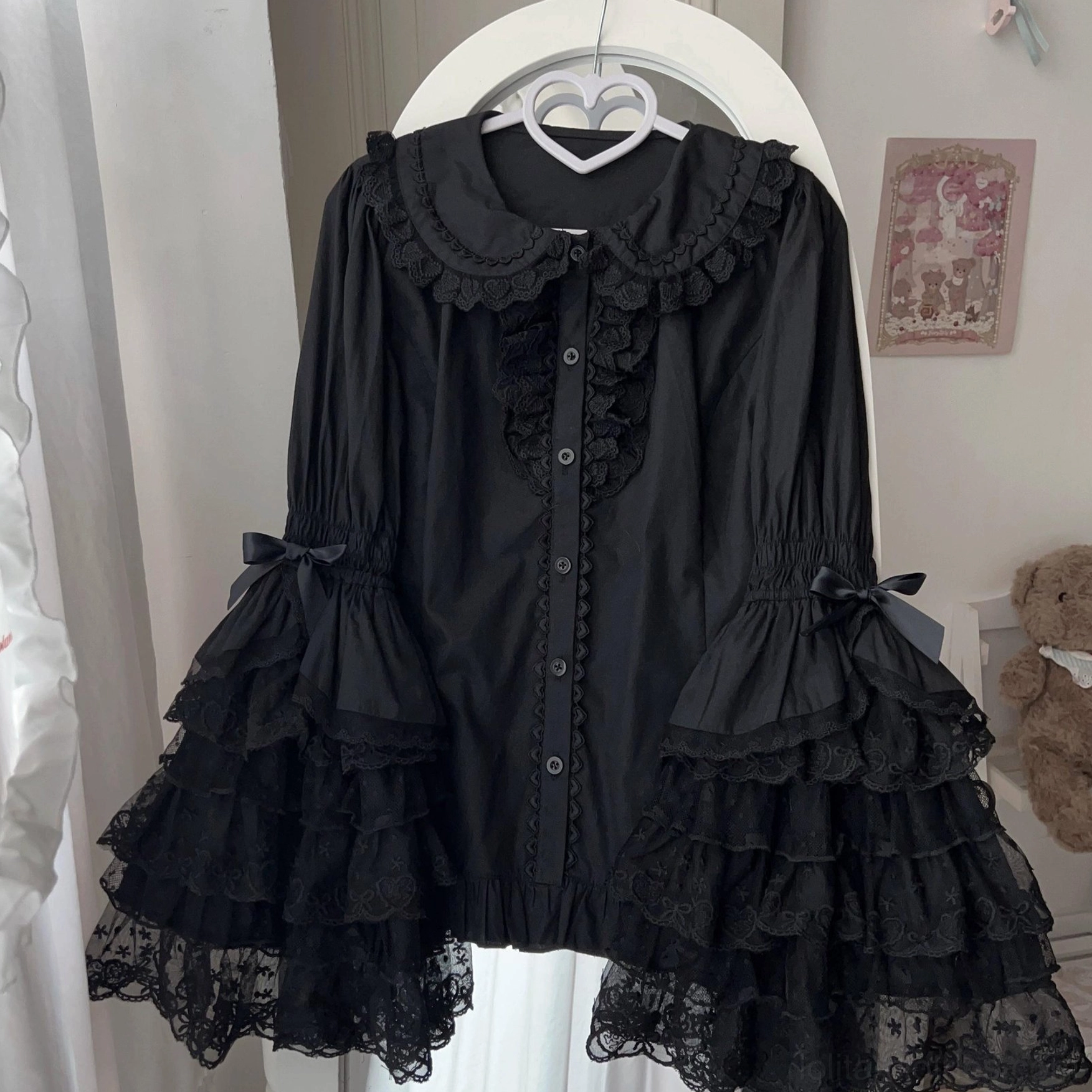 Black Sweet Lolita blouse with delicate Peter Pan collar lace trim and ruffled lace trumpet sleeves with bow cuffs, elegant hanging display on white background