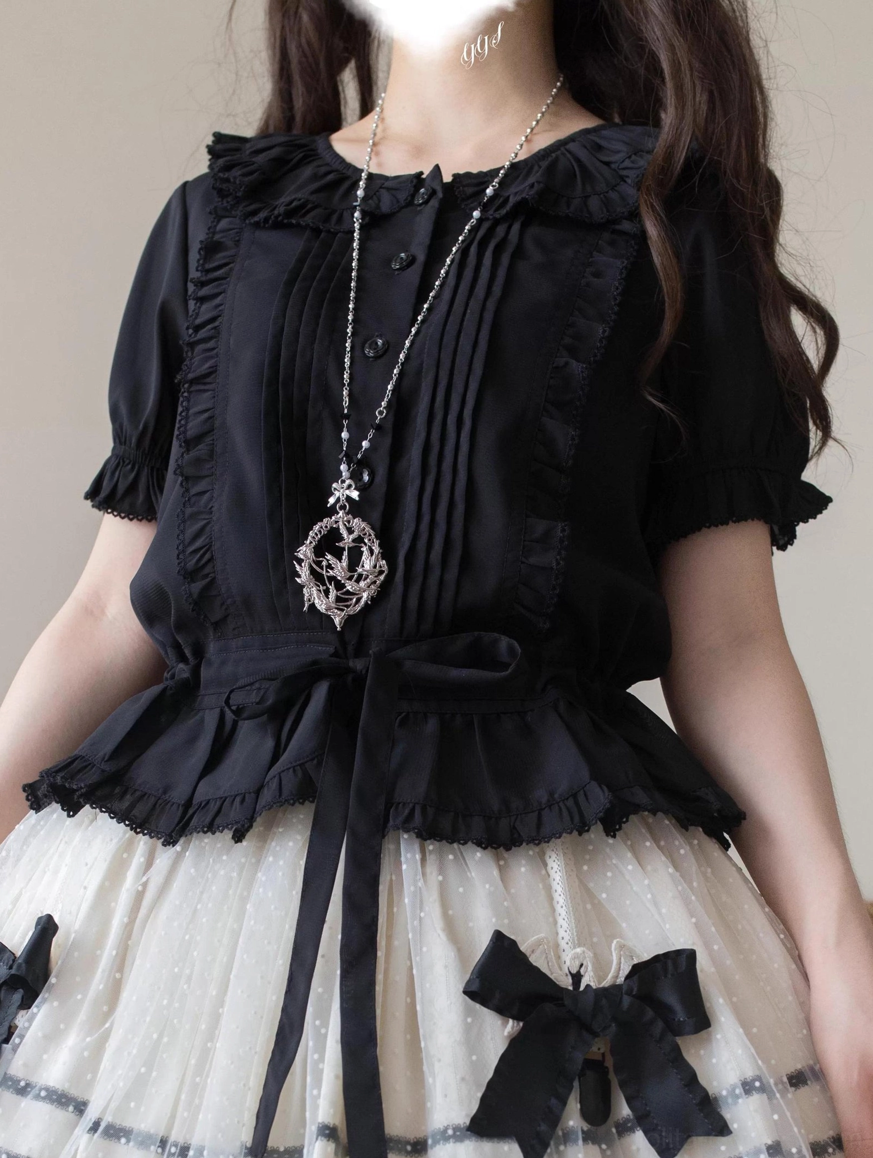 Black sweet Lolita blouse front close-up displaying ruffled Peter Pan collar, front pintuck trims, large waist bow sash, short ruffled sleeves, and button placket