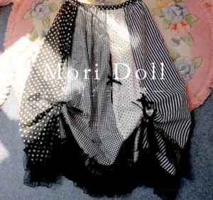 Black sweet lolita skirt top-down flat lay view showing dark color block patchwork design with mixed polka dot stripe and gingham fabrics black tulle hem and black bow decorations on floral rug