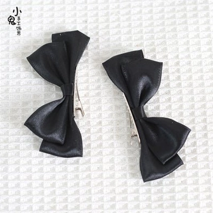 Black Sweet Lolita satin bow hair clips flat lay on checkered fabric background showing classic double bow design with metal clips and rich black satin finish