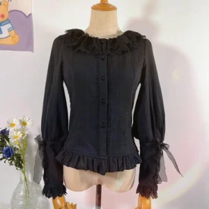 Black plus-size velvet lolita long-sleeve blouse with lace ruffled collar, front button placket, ruffled hem, and lace-trimmed bell sleeves with ribbon ties, displayed on dress mannequin in studio setting with floral decorations