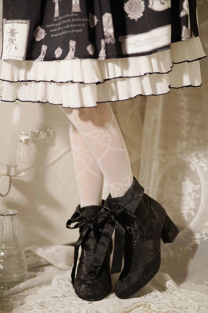 Close-up partial lower body view of black lolita ankle boots with ruffled black and white lolita skirt highlighting lace-up ribbon bow closure matte black fabric and block heel construction