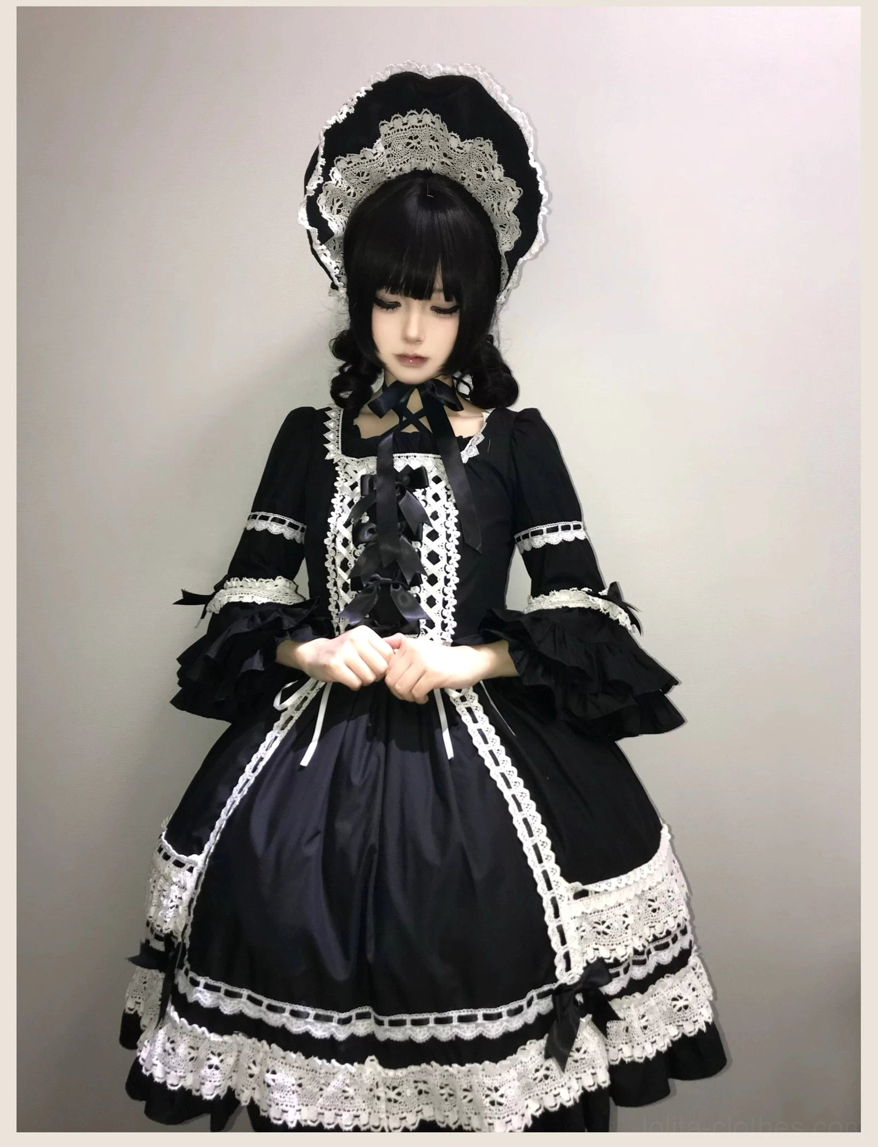 Close-up studio view of black old school lolita dress upper body showing square neckline, white lace-up front, puff sleeves with lace trim, and waist bow decoration
